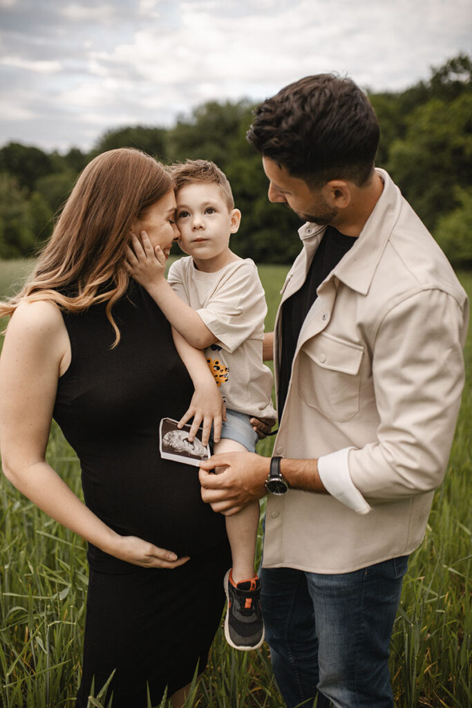 Babybauchshooting auf einem Feld bei Wiener Neustadt: Eltern halten Kind mit Ultraschallbild.