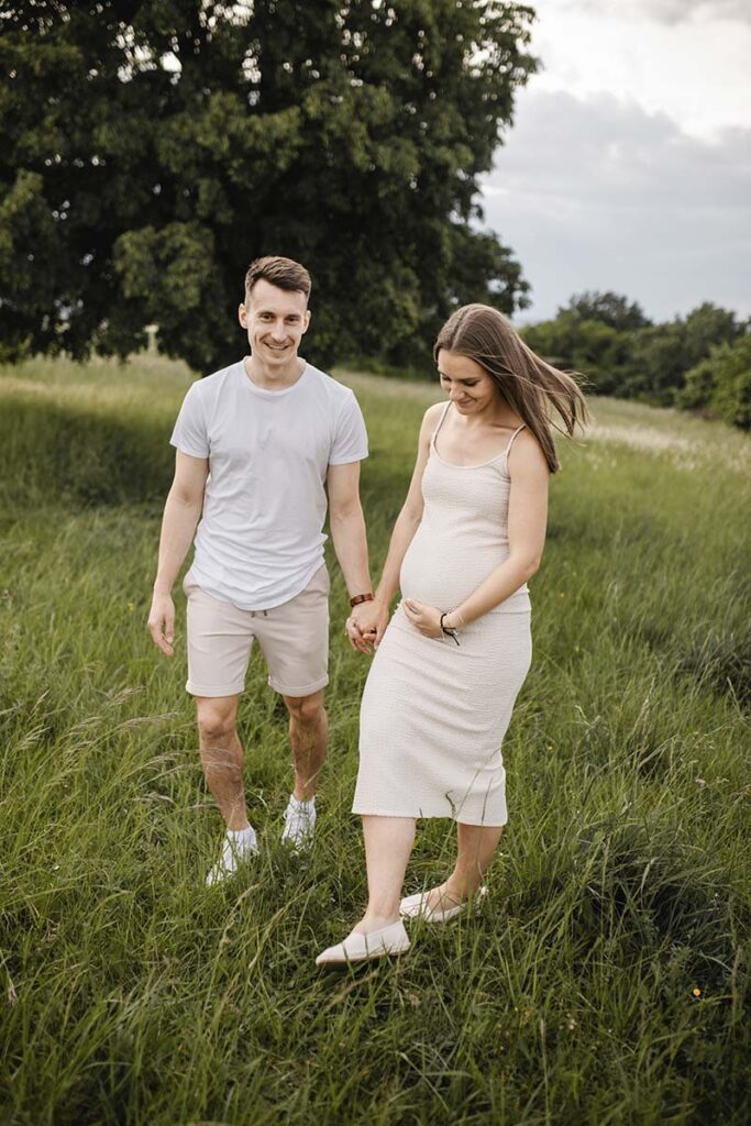 Schwangere Frau hält ihren Babybauch auf einem Feld und strahlt Vorfreude aus.