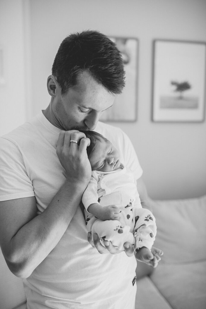Baby schläft in Papas Armen – entspannter Augenblick beim Newborn Shooting zuhause