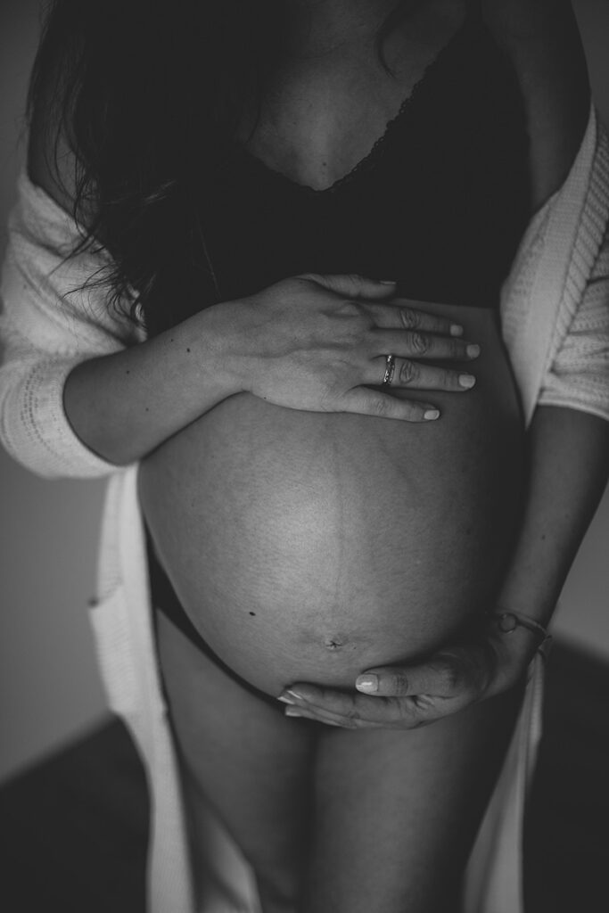 Schwarzweißaufnahme: Schwangere Frau hält ihren Babybauch bei einer Homestory zuhause.