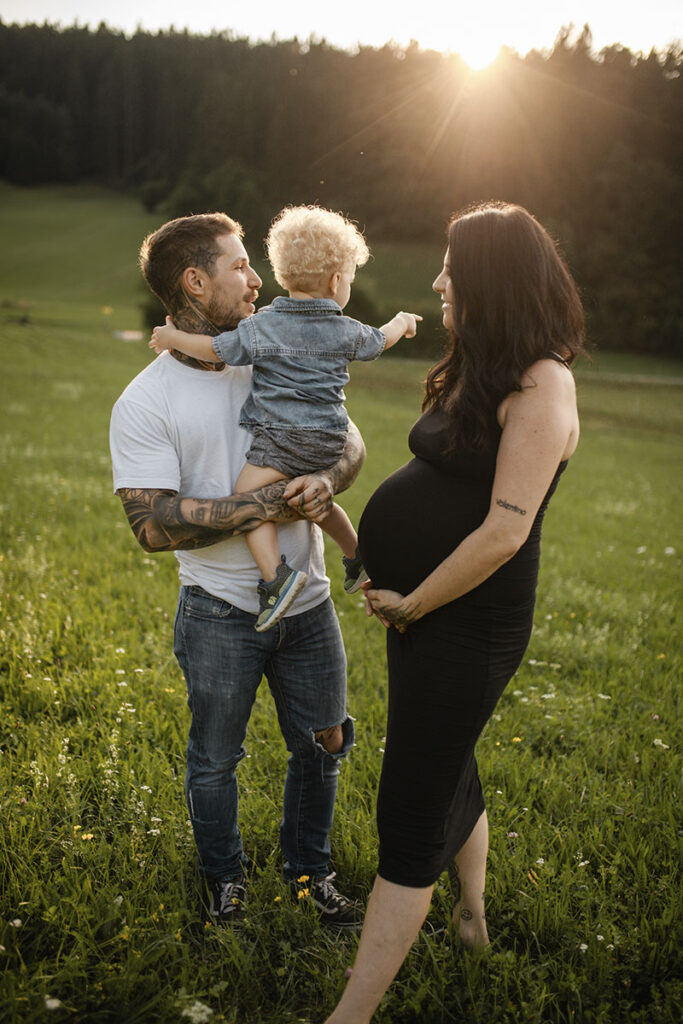 Familie auf einem Frühlingsfeld mit Kleinkind und Babybauch bei Sonnenuntergang.