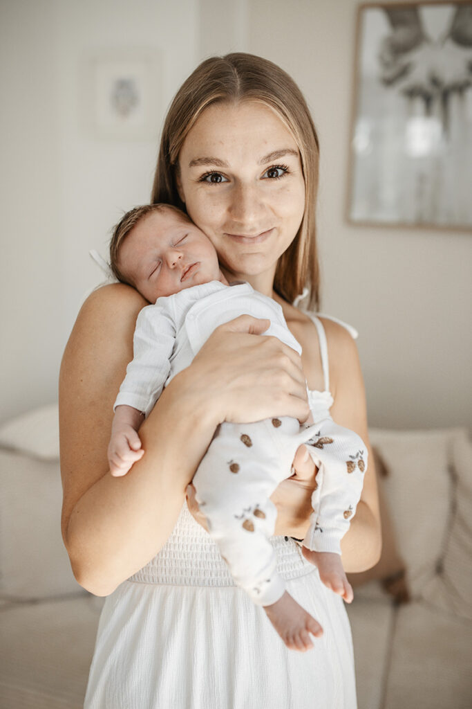 Mama hält ihr Neugeborenes im Wohnzimmer beim ruhigen Homeshooting in Wr. Neustadt