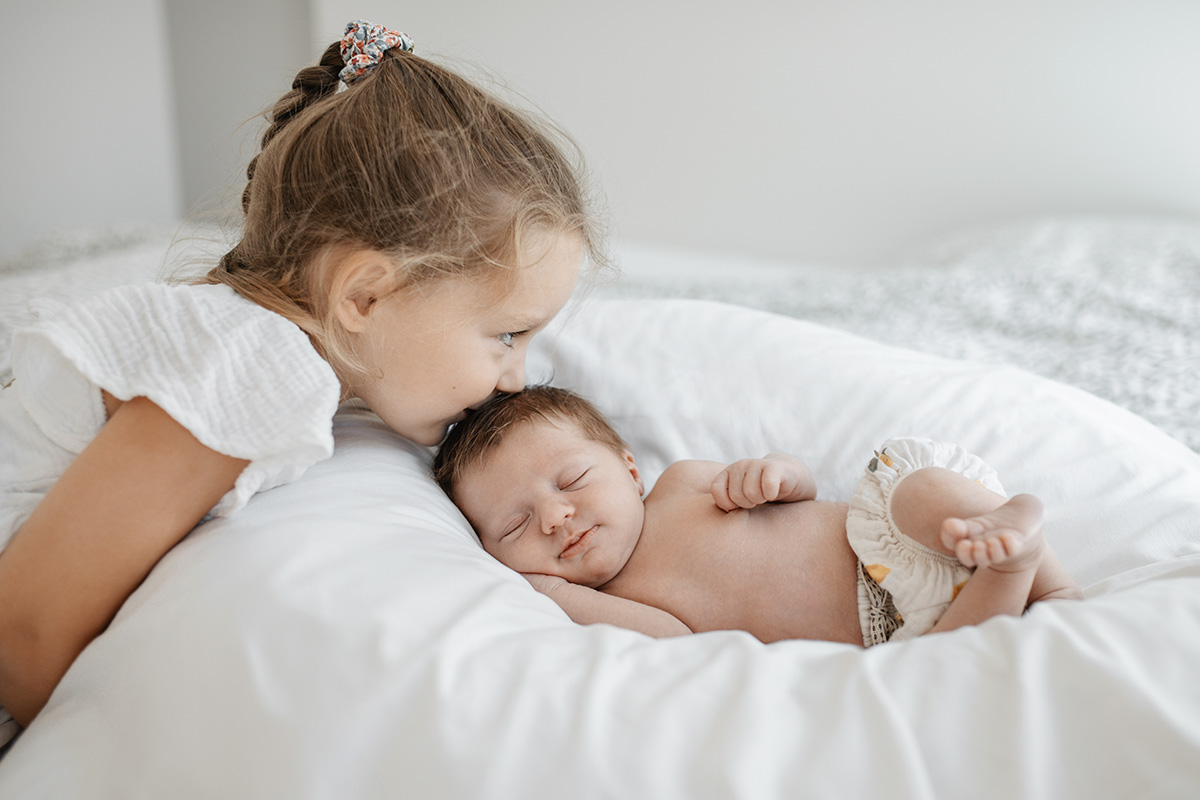 Neugeborenes Baby mit Geschwisterkind auf Decke im Wohnzimmer beim natürlichen Babyshooting zuhause