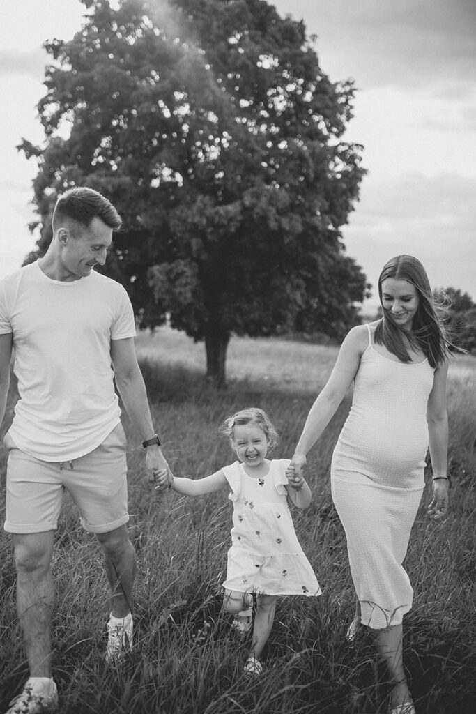 Familie mit Kleinkind läuft über eine Wiese bei einem Babybauchshooting.