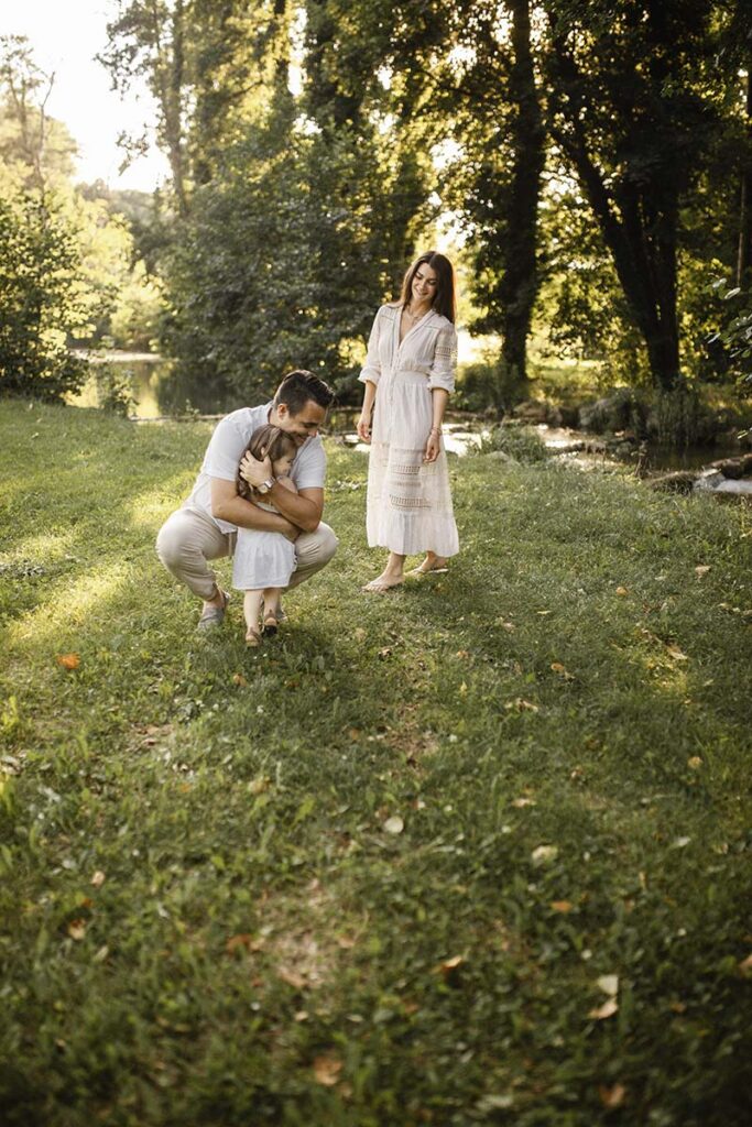 Innige Umarmung zwischen Vater und Tochter im Sonnenlicht, während die Mutter voller Freude zusieht.