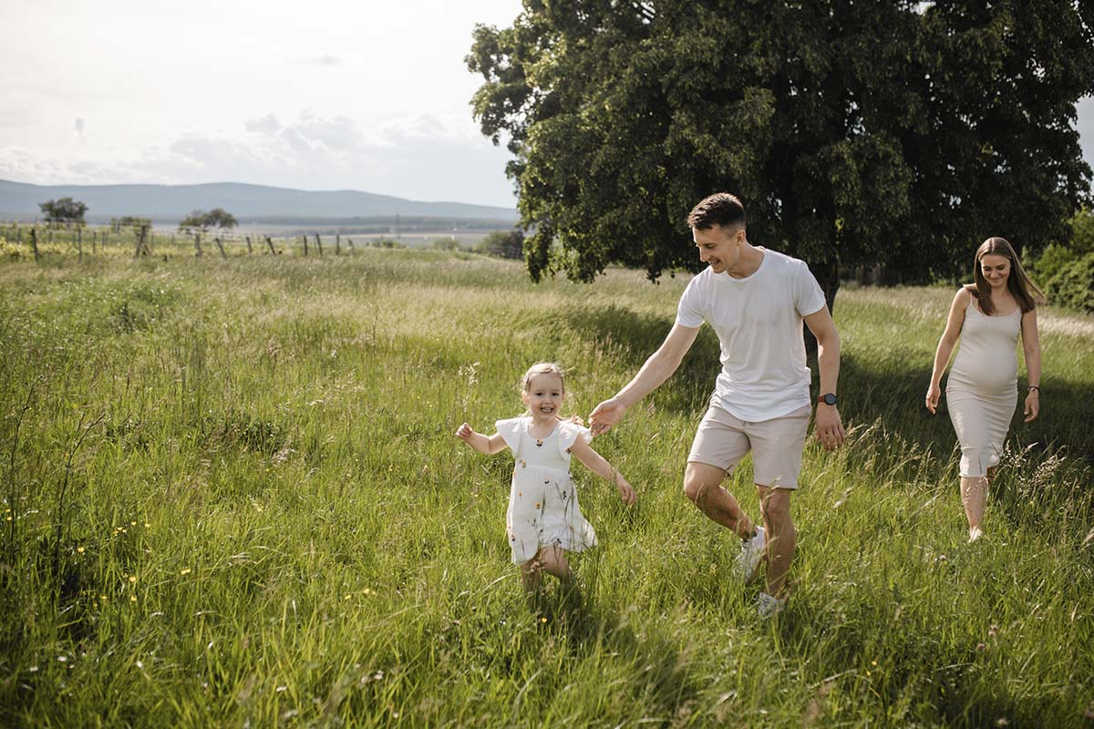 wiese-babybauch-familienfotos-wiener-neustadt Werdende Eltern und Kind genießen einen Sommertag bei ihrem Babybauchshooting in Wiener Neustadt.