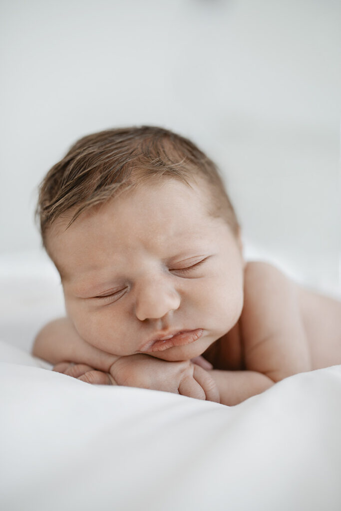 Schlafendes zwei Wochen altes Baby mit Kopf auf Armen bei einem Shooting zuhause.